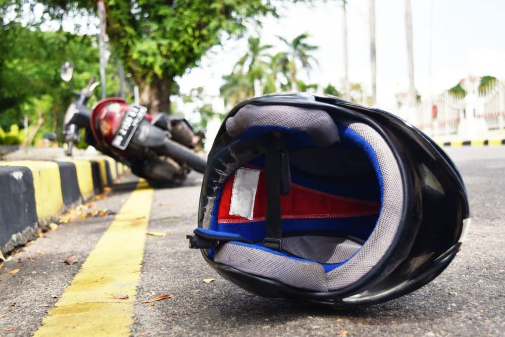 A motorcycle helmet lies behind a fallen motorcycle on the side of the road.