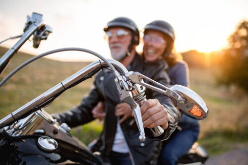 An older couple sitting on a black and chrome motorcycle with helmets on.