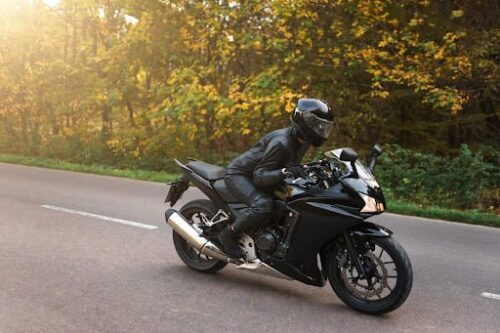 A biker in all black on a black motorcycle, driving down the road.
